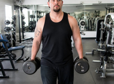 Man carrying heavy dumbbells through a budget gym early in the morning