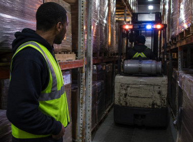 Narrow warehouse aisle with forklift barely fitting between tall racking at night