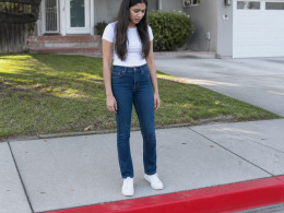 South Asian woman in white t-shirt looking puzzled at fresh red curb with no parking stencil in front of suburban house.