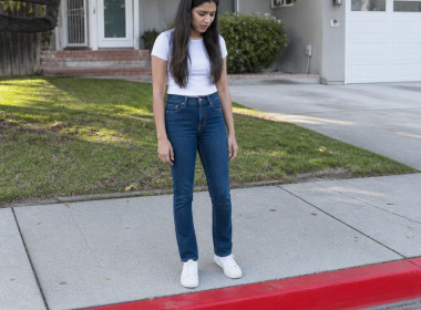 South Asian woman in white t-shirt looking puzzled at fresh red curb with no parking stencil in front of suburban house.