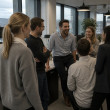 Popular manager surrounded by laughing coworkers while one woman looks slightly uncertain