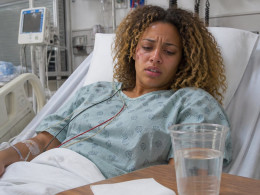 Patient lying in hospital bed with medical monitors and a rideshare receipt on the bedside table.