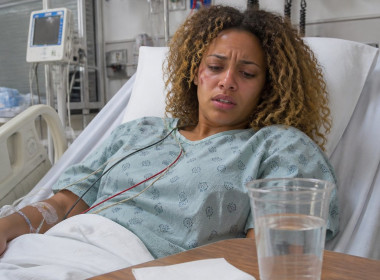 Patient lying in hospital bed with medical monitors and a rideshare receipt on the bedside table.
