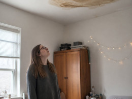 Young woman looking up at water stain on her bedroom ceiling above the bed