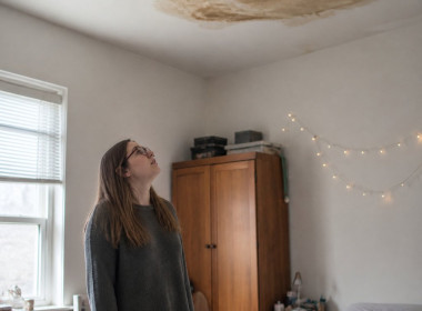 Young woman looking up at water stain on her bedroom ceiling above the bed