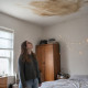 Young woman looking up at water stain on her bedroom ceiling above the bed