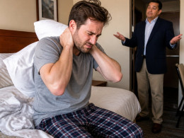 Man in hospital bed struggling to lift his head while ER doctor listens to his chest.