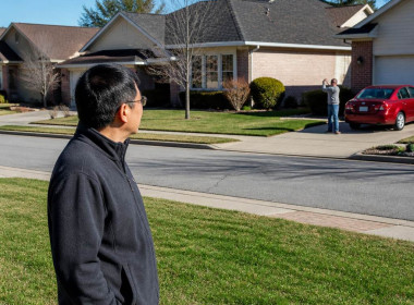 Man on lawn watching neighbor filming rooftop solar panels from driveway.
