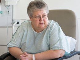 Concerned patient in hospital gown sitting in recovery room recliner.