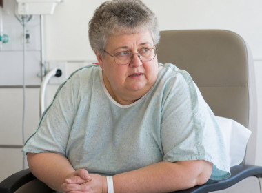 Concerned patient in hospital gown sitting in recovery room recliner.