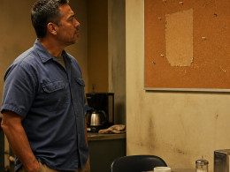 Man in blue work shirt looking at empty corkboard in break room