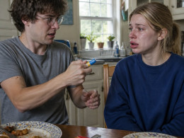 Man administering EpiPen to woman with swollen lips at kitchen table