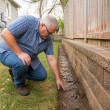 Man inspecting damp soil line by fence near retaining wall in backyard.