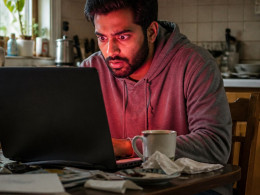Man looking anxiously at a glowing laptop screen in a dim kitchen.
