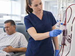 Nurse observing tea-colored blood in dialysis venous line as patient shows discomfort