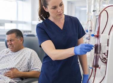 Nurse observing tea-colored blood in dialysis venous line as patient shows discomfort