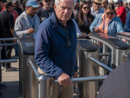 Man in blue jacket at locked turnstile with frustrated expression, surrounded by waiting crowd.