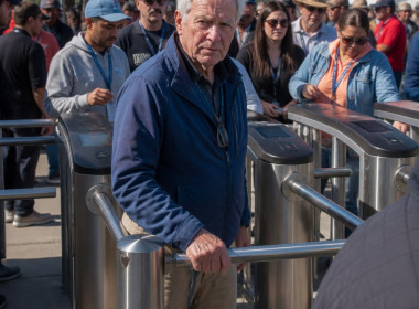 Man in blue jacket at locked turnstile with frustrated expression, surrounded by waiting crowd.