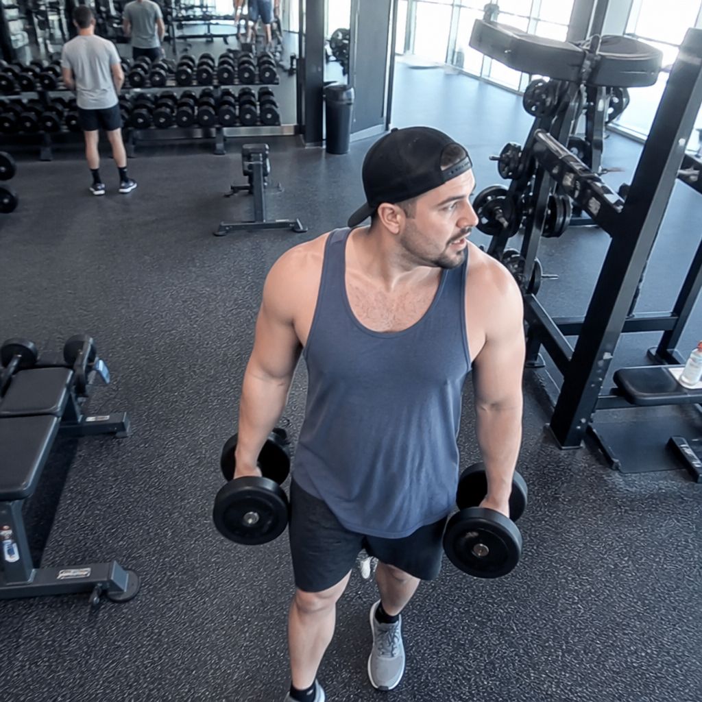 Gym surveillance angle showing man carrying dumbbells while looking away distracted